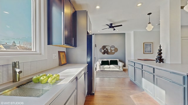 kitchen with hanging light fixtures, a sink, light wood-style floors, backsplash, and recessed lighting