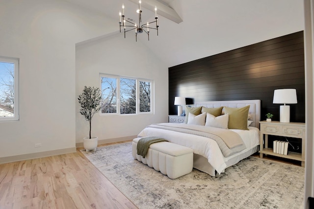 bedroom with high vaulted ceiling, a notable chandelier, an accent wall, wood finished floors, and baseboards