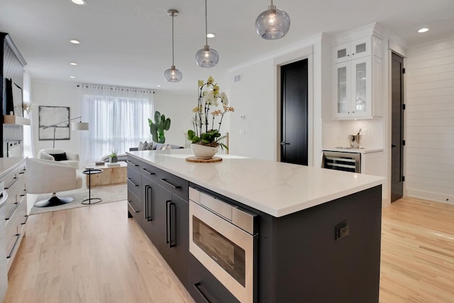 kitchen with open floor plan, light wood finished floors, stainless steel microwave, and white cabinetry