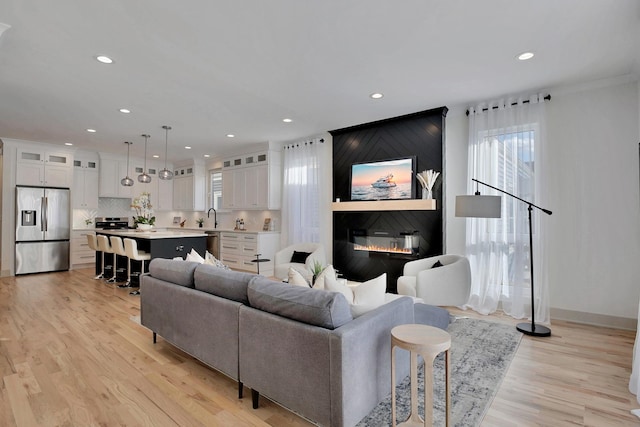 living room with a large fireplace, light wood-type flooring, baseboards, and recessed lighting