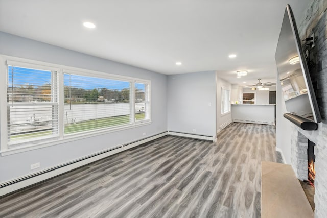 unfurnished living room with a baseboard heating unit, a baseboard radiator, a healthy amount of sunlight, and wood finished floors