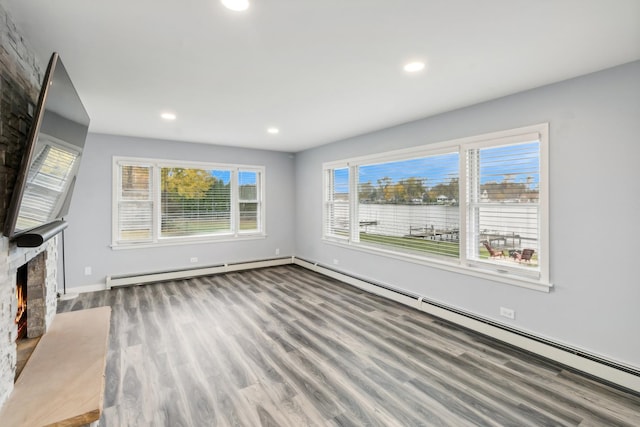 unfurnished living room with recessed lighting, a baseboard heating unit, a large fireplace, wood finished floors, and baseboards