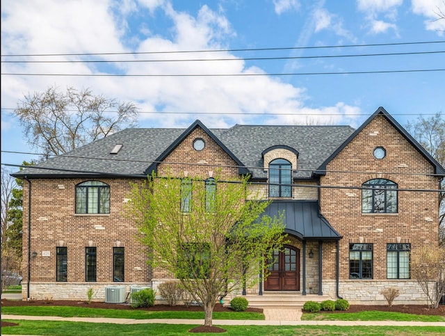 french country style house featuring stone siding, brick siding, cooling unit, and roof with shingles