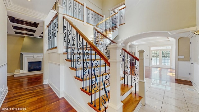 stairs with arched walkways, decorative columns, a high ceiling, a glass covered fireplace, and hardwood / wood-style flooring