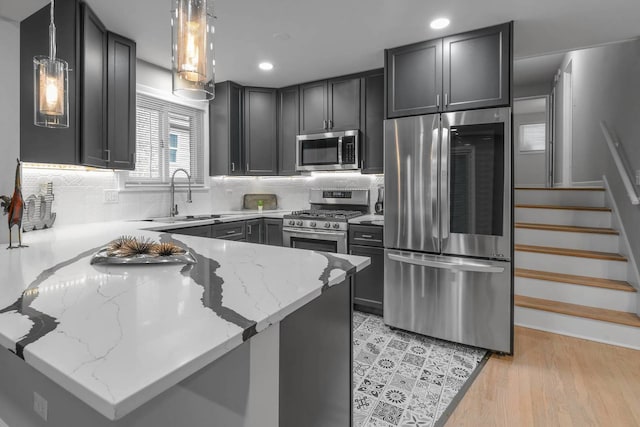 kitchen with a peninsula, light stone countertops, stainless steel appliances, light wood-type flooring, and a sink