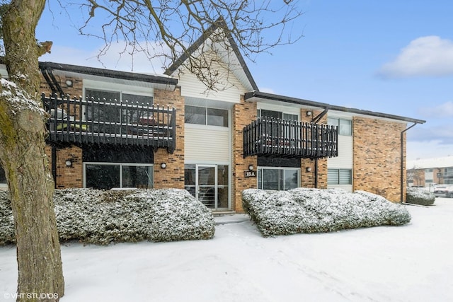 snow covered house with a balcony and brick siding