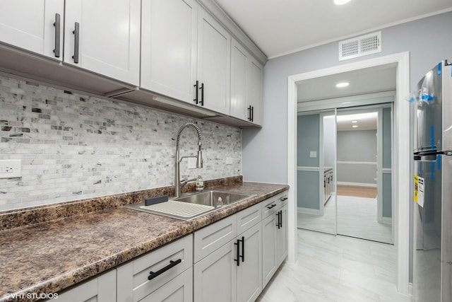 kitchen featuring visible vents, backsplash, freestanding refrigerator, a sink, and baseboards