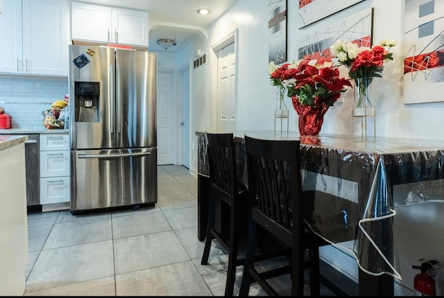 kitchen with light tile patterned floors, visible vents, white cabinets, stainless steel refrigerator with ice dispenser, and backsplash