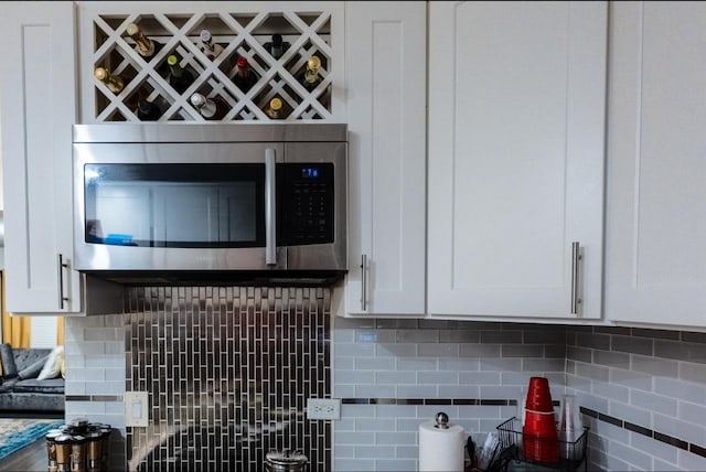 kitchen with tasteful backsplash, stainless steel microwave, and white cabinetry