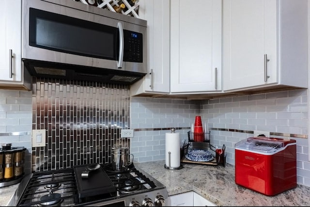 kitchen featuring white cabinets, decorative backsplash, range, stainless steel microwave, and light stone counters