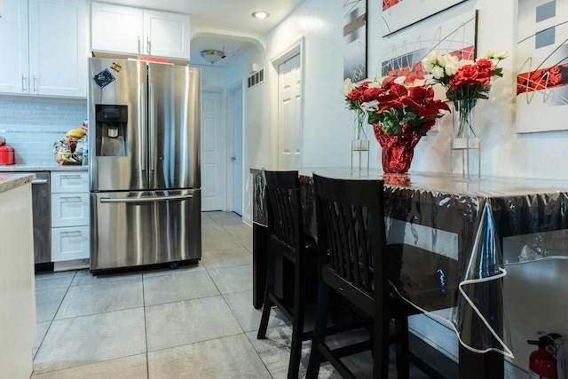 kitchen with light tile patterned floors, stainless steel fridge, tasteful backsplash, visible vents, and white cabinets