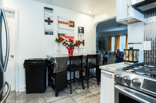 kitchen featuring stainless steel gas stove, white cabinets, refrigerator, under cabinet range hood, and backsplash