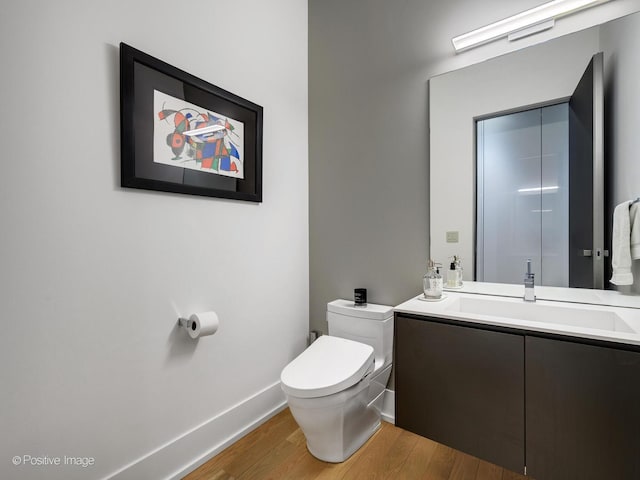 half bathroom featuring toilet, baseboards, wood finished floors, and vanity