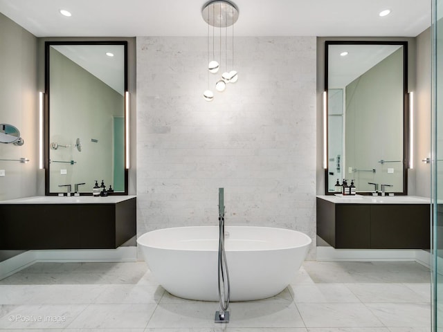 bathroom with marble finish floor, tile walls, recessed lighting, two vanities, and a freestanding tub