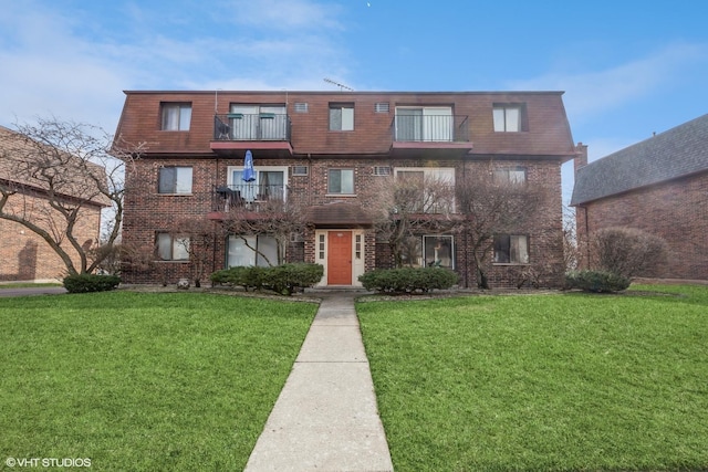 view of front of property with brick siding, a balcony, and a front yard