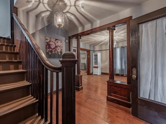 stairs featuring a chandelier, decorative columns, and wood finished floors