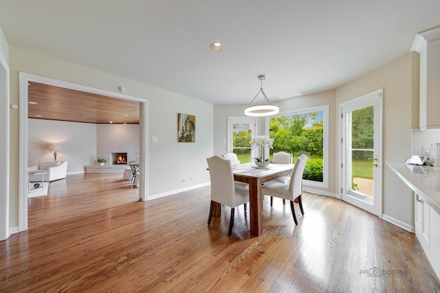 dining area featuring a wealth of natural light, a lit fireplace, light wood-style flooring, and baseboards