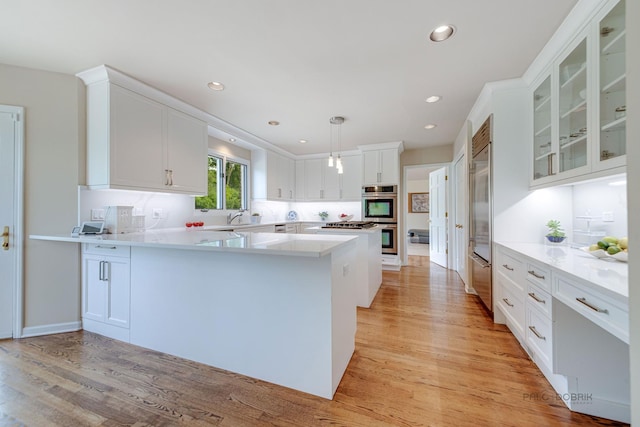 kitchen with stainless steel appliances, light wood finished floors, a peninsula, and white cabinetry