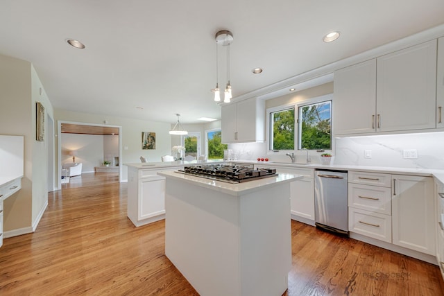 kitchen featuring a peninsula, a kitchen island, light countertops, light wood finished floors, and stainless steel gas stovetop