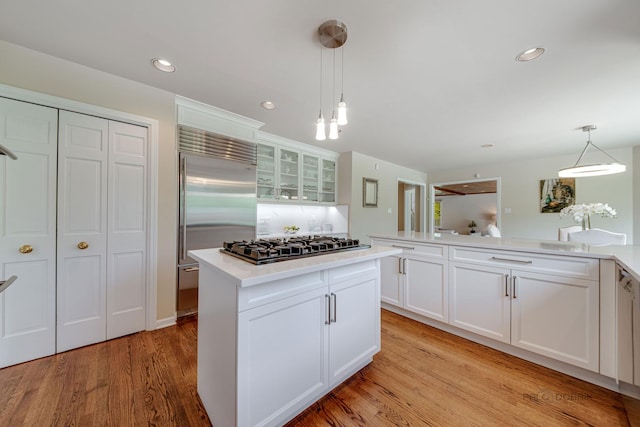 kitchen featuring built in fridge, gas stovetop, white cabinets, light wood finished floors, and glass insert cabinets