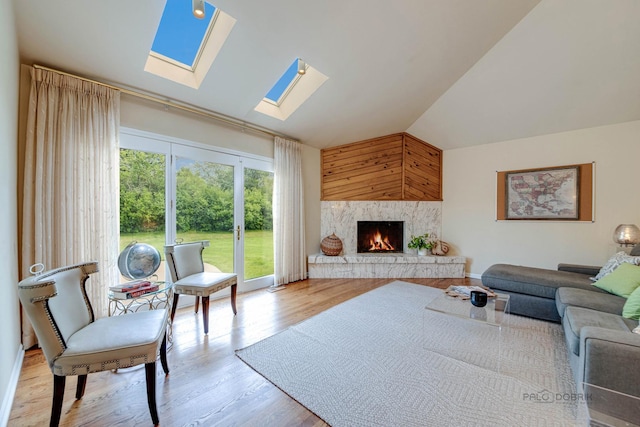 living room featuring a warm lit fireplace, lofted ceiling with skylight, and wood finished floors