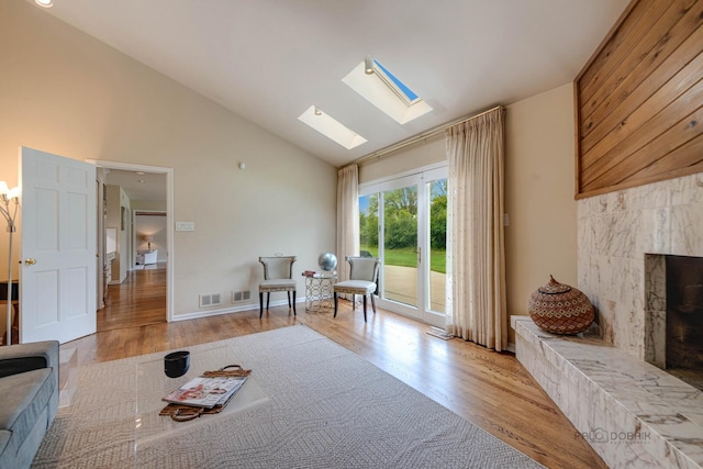 living area with high vaulted ceiling, a fireplace, wood finished floors, a skylight, and visible vents