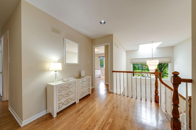 corridor featuring a chandelier, light wood-style flooring, visible vents, and a wealth of natural light