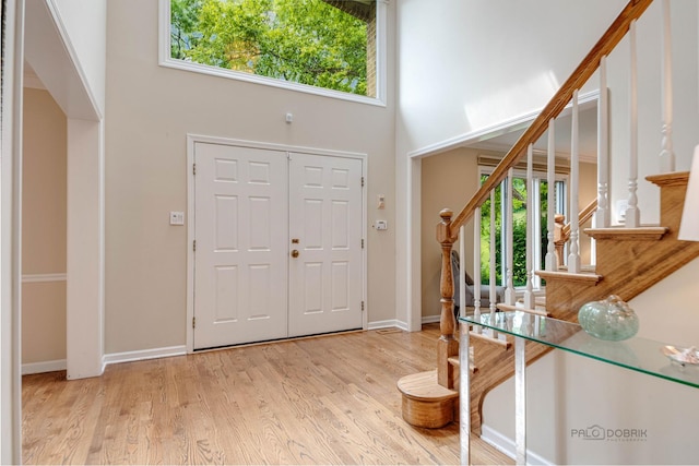 foyer entrance featuring a towering ceiling, baseboards, stairway, and wood finished floors