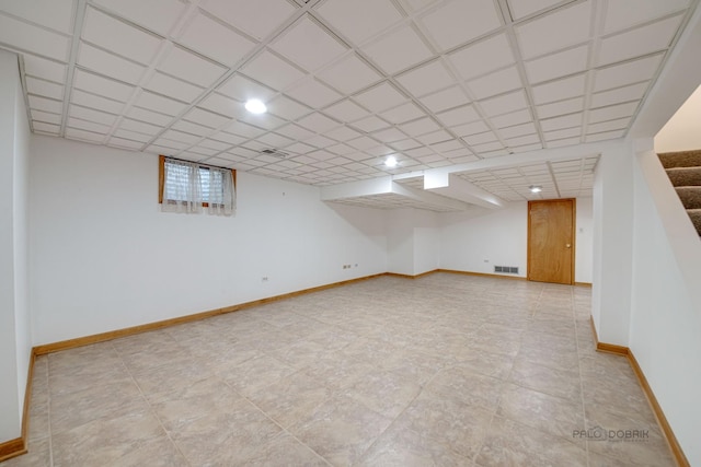 finished basement with visible vents, stairway, baseboards, and a drop ceiling