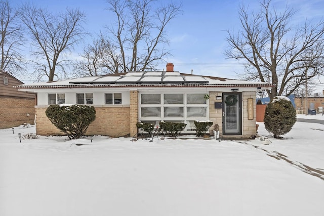 single story home featuring brick siding, a chimney, and solar panels