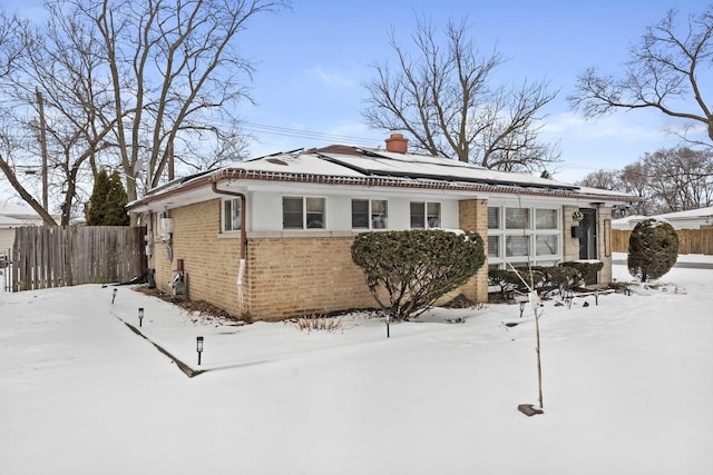 view of front facade featuring a chimney, fence, solar panels, and brick siding