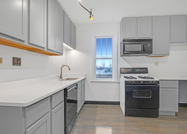 kitchen featuring gray cabinetry, a sink, light countertops, black appliances, and dark wood finished floors