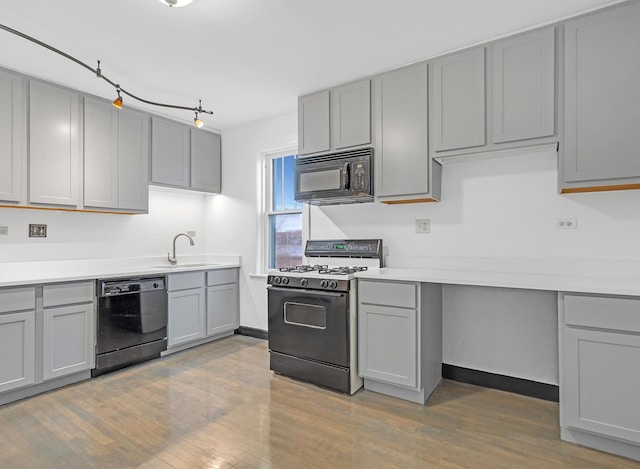 kitchen with wood finished floors, light countertops, gray cabinetry, black appliances, and a sink