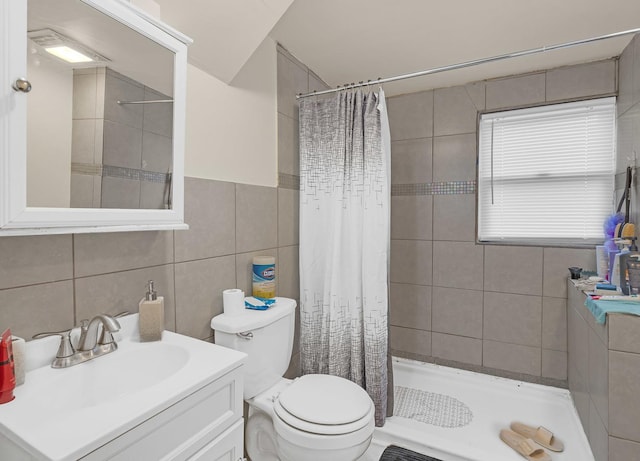 bathroom with toilet, tiled shower, vanity, and tile walls