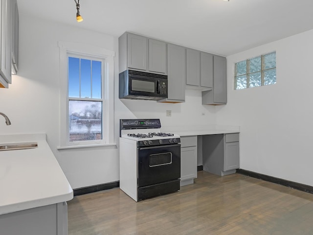 kitchen featuring range with gas cooktop, a wealth of natural light, gray cabinets, a sink, and black microwave