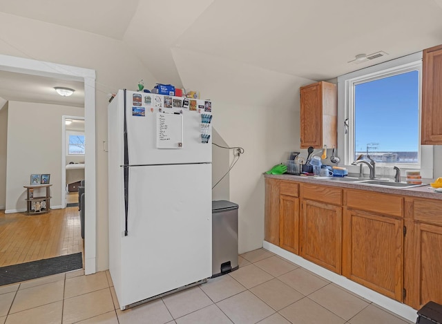 kitchen with light tile patterned flooring, a sink, vaulted ceiling, freestanding refrigerator, and brown cabinets