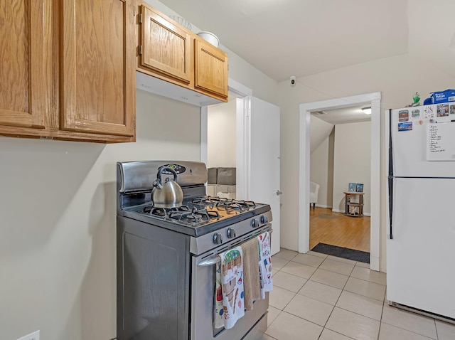 kitchen with gas range, under cabinet range hood, light tile patterned flooring, and freestanding refrigerator