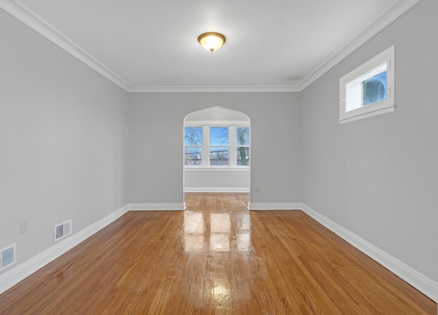 spare room featuring arched walkways, visible vents, plenty of natural light, and wood finished floors