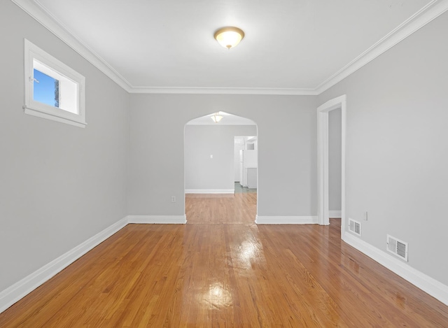 spare room with light wood finished floors, baseboards, visible vents, and arched walkways