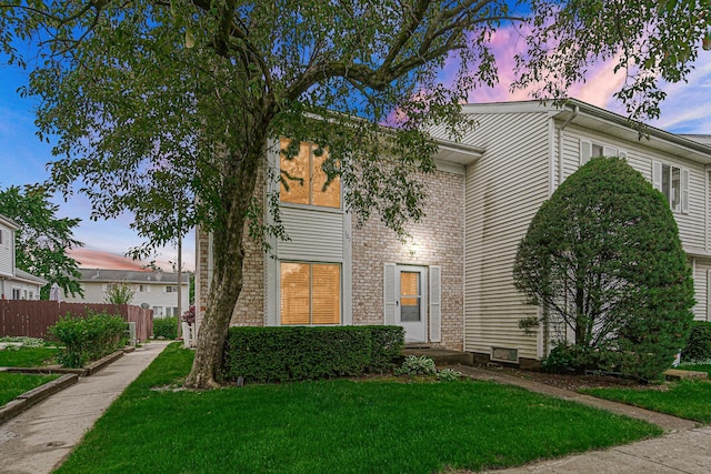 view of front facade featuring a yard, brick siding, and fence