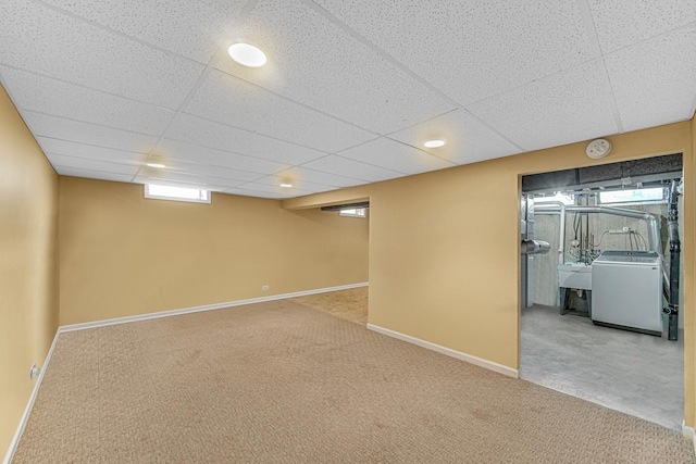 basement featuring a paneled ceiling, carpet floors, a sink, baseboards, and washer / clothes dryer