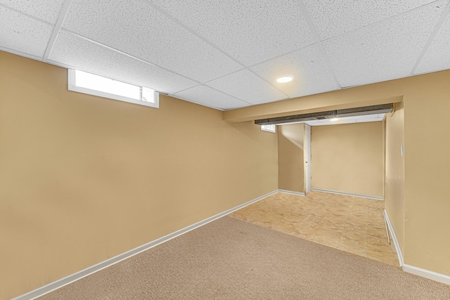 basement with carpet floors, a paneled ceiling, and baseboards