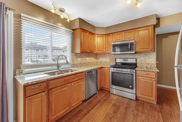 kitchen with light stone counters, wood finished floors, a sink, appliances with stainless steel finishes, and backsplash