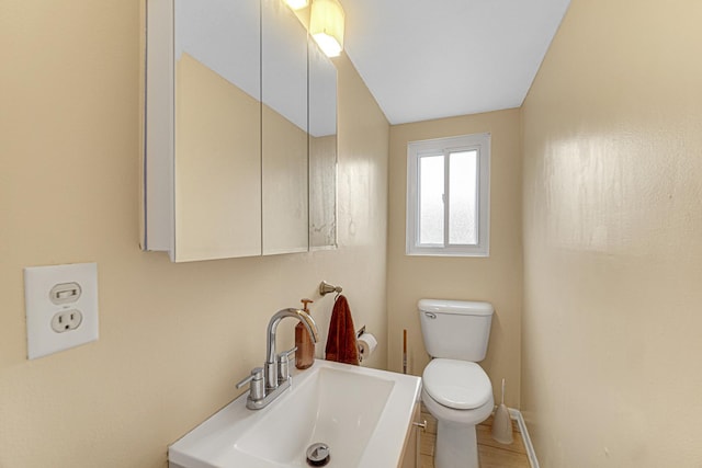 half bath with toilet, baseboards, and vanity