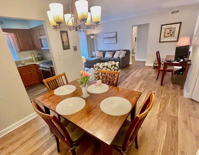 dining room featuring baseboards, visible vents, light wood finished floors, and an inviting chandelier