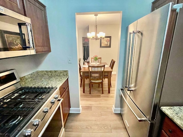 kitchen with stainless steel appliances, an inviting chandelier, light wood finished floors, and light stone countertops