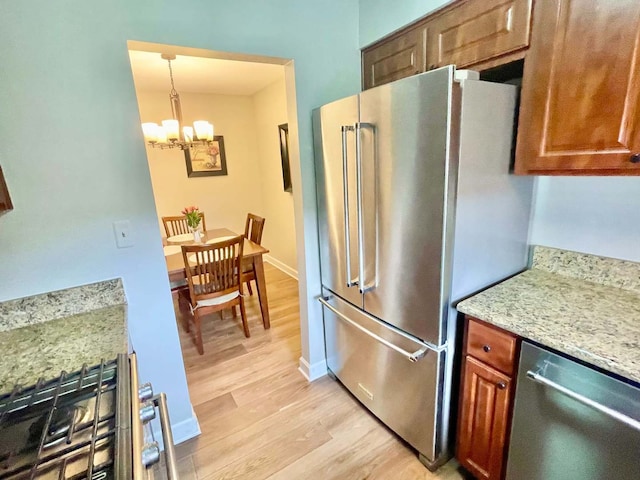 kitchen featuring stainless steel appliances, baseboards, brown cabinets, light stone countertops, and light wood finished floors