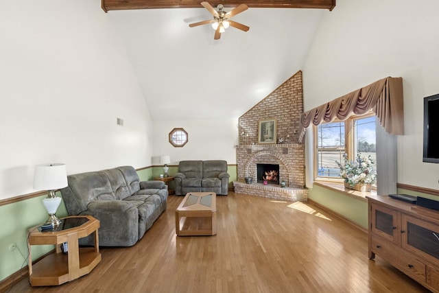 living room with beam ceiling, a fireplace, light wood-style floors, a ceiling fan, and high vaulted ceiling