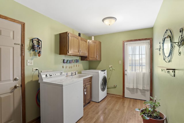 washroom featuring cabinet space, baseboards, light wood-type flooring, washing machine and dryer, and a sink