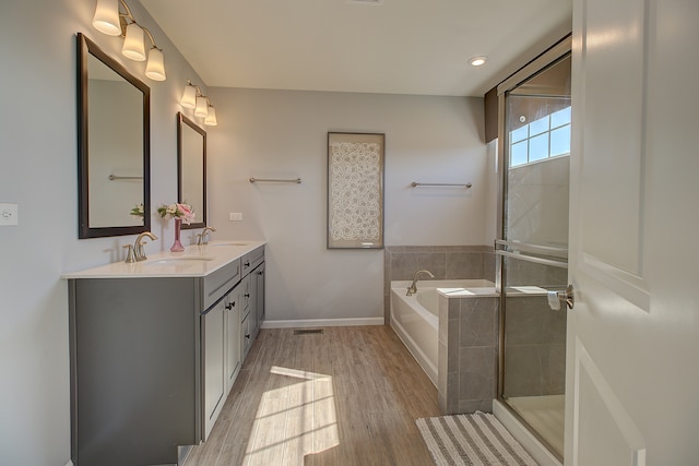 bathroom featuring a garden tub, double vanity, wood finished floors, and a sink